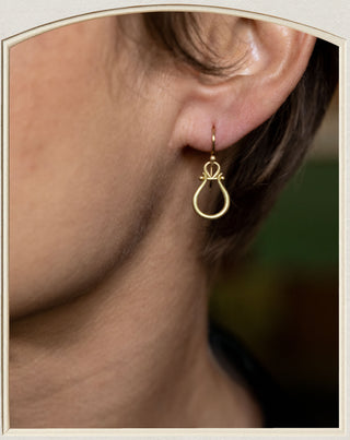 A close-up of a person's ear wearing a delicate gold hoop earring with a small teardrop-shaped drop.