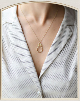 A delicate gold teardrop pendant necklace worn by a model in a white button-down shirt with a subtle black polka dot pattern.