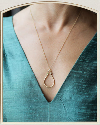 A delicate gold necklace with a teardrop-shaped pendant and a small star detail at the top, shown worn on a model's neck over a textured teal green V-neck top.