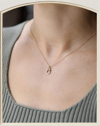 A delicate gold necklace with a small ring pendant, worn on a model's neck over a ribbed gray top.