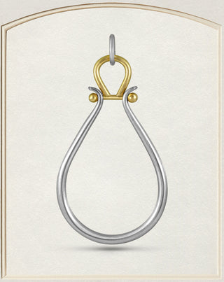 A two-tone metal pendant with a silver teardrop-shaped loop and a gold-colored top loop and side accents, displayed on a textured cream background.