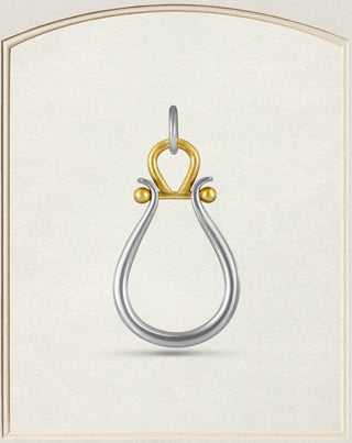 A two-tone metal pendant featuring a silver teardrop-shaped loop with a gold top loop and small gold accent beads, displayed on a textured cream background.