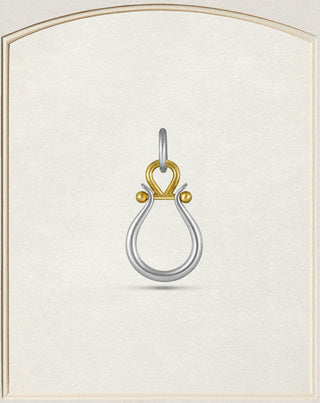 A two-tone metal pendant featuring a silver teardrop loop and a gold heart-shaped top with small gold beads, centered on a textured cream background with a decorative border.